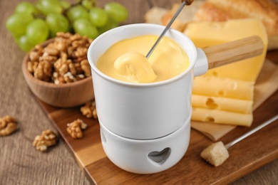 Pot of tasty cheese fondue and fork with bread on wooden table