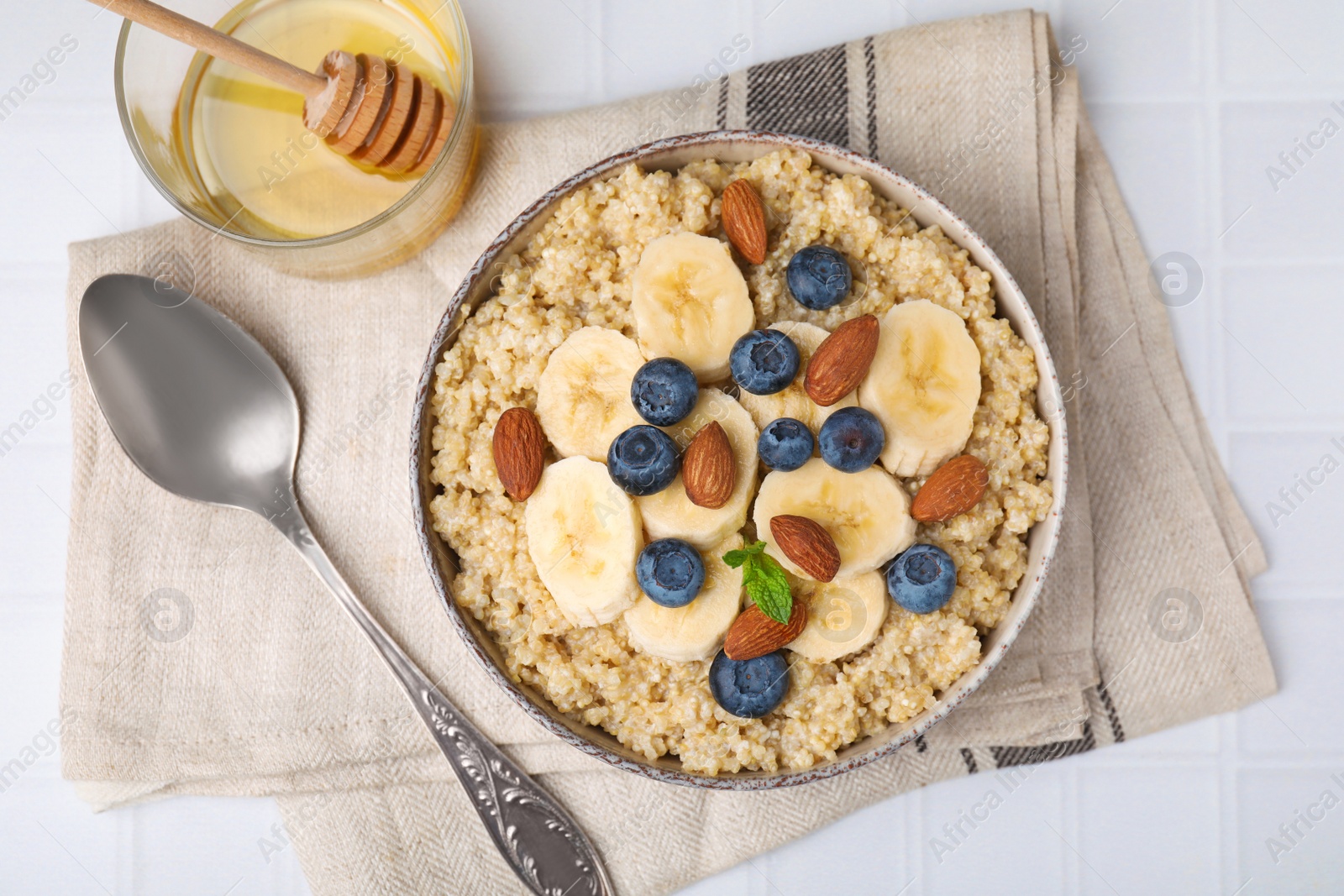 Photo of Bowl of delicious cooked quinoa with almonds, bananas and blueberries on white table, flat lay