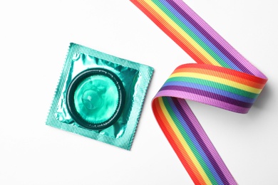 Photo of Green condom and rainbow ribbon on white background, top view. LGBT concept