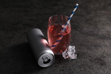 Photo of Energy drink in glass, aluminium can and ice cubes on grey table