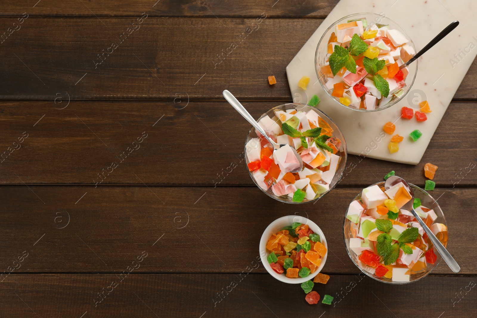 Photo of Delicious broken glass jelly dessert on wooden table, flat lay. Space for text