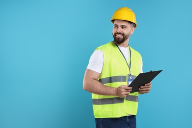 Photo of Engineer in hard hat holding clipboard on light blue background, space for text