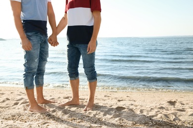 Photo of Gay couple standing barefoot on beach. Space for text