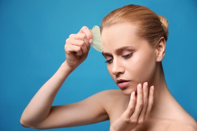 Photo of Beautiful young woman doing facial massage with gua sha tool on blue background