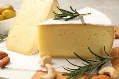 Photo of Pieces of tasty camembert cheese, rosemary and nuts on table, closeup