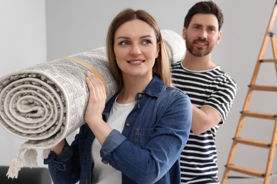 Photo of Smiling couple holding rolled carpet in room