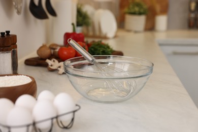 Photo of Metal whisk, bowl and different products on light table in kitchen