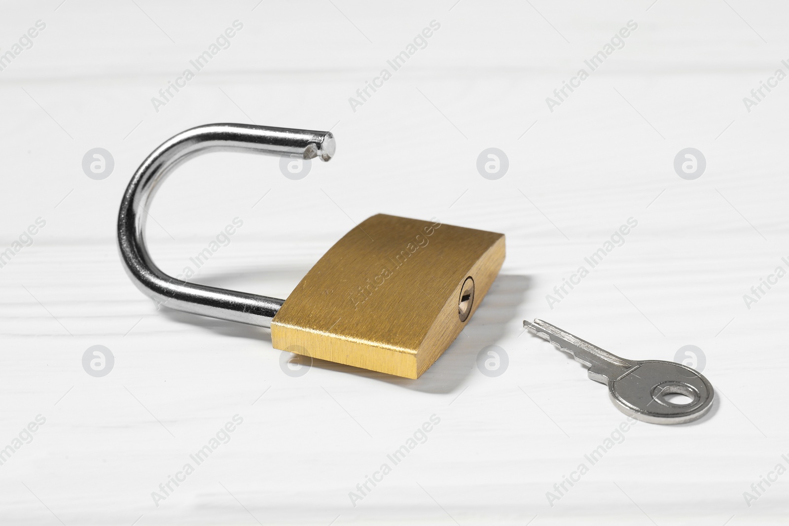 Photo of Steel padlock with key on white wooden table, closeup