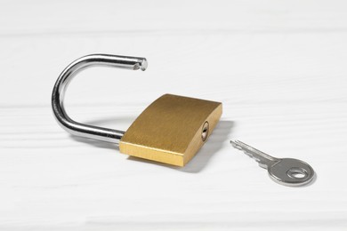 Steel padlock with key on white wooden table, closeup