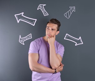 Image of Choice in profession or other areas of life, concept. Making decision, thoughtful young man surrounded by drawn arrows on grey background
