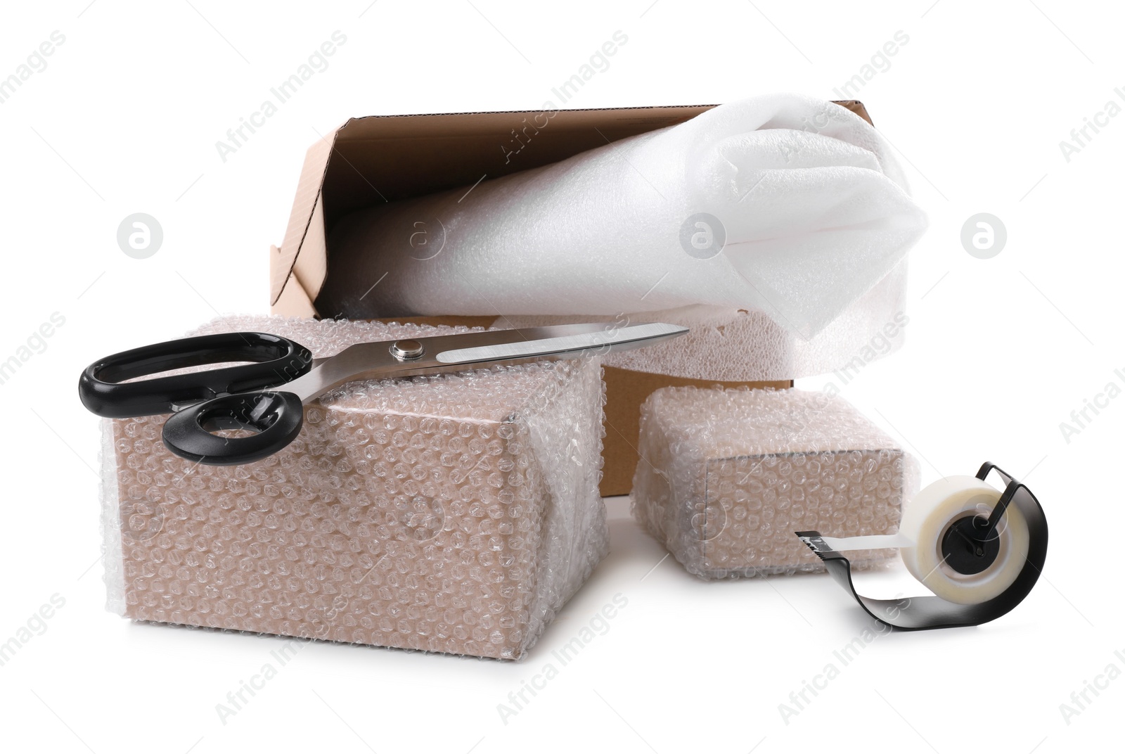 Photo of Cardboard boxes packed in bubble wrap, scissors and adhesive tape on white background