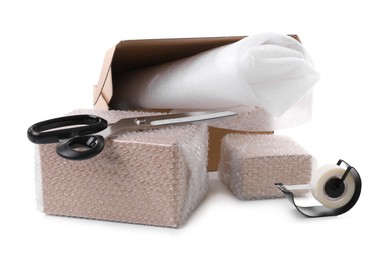 Cardboard boxes packed in bubble wrap, scissors and adhesive tape on white background