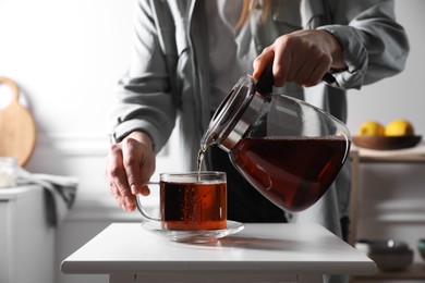 Photo of Woman pouring hot tea into cup at white table, closeup