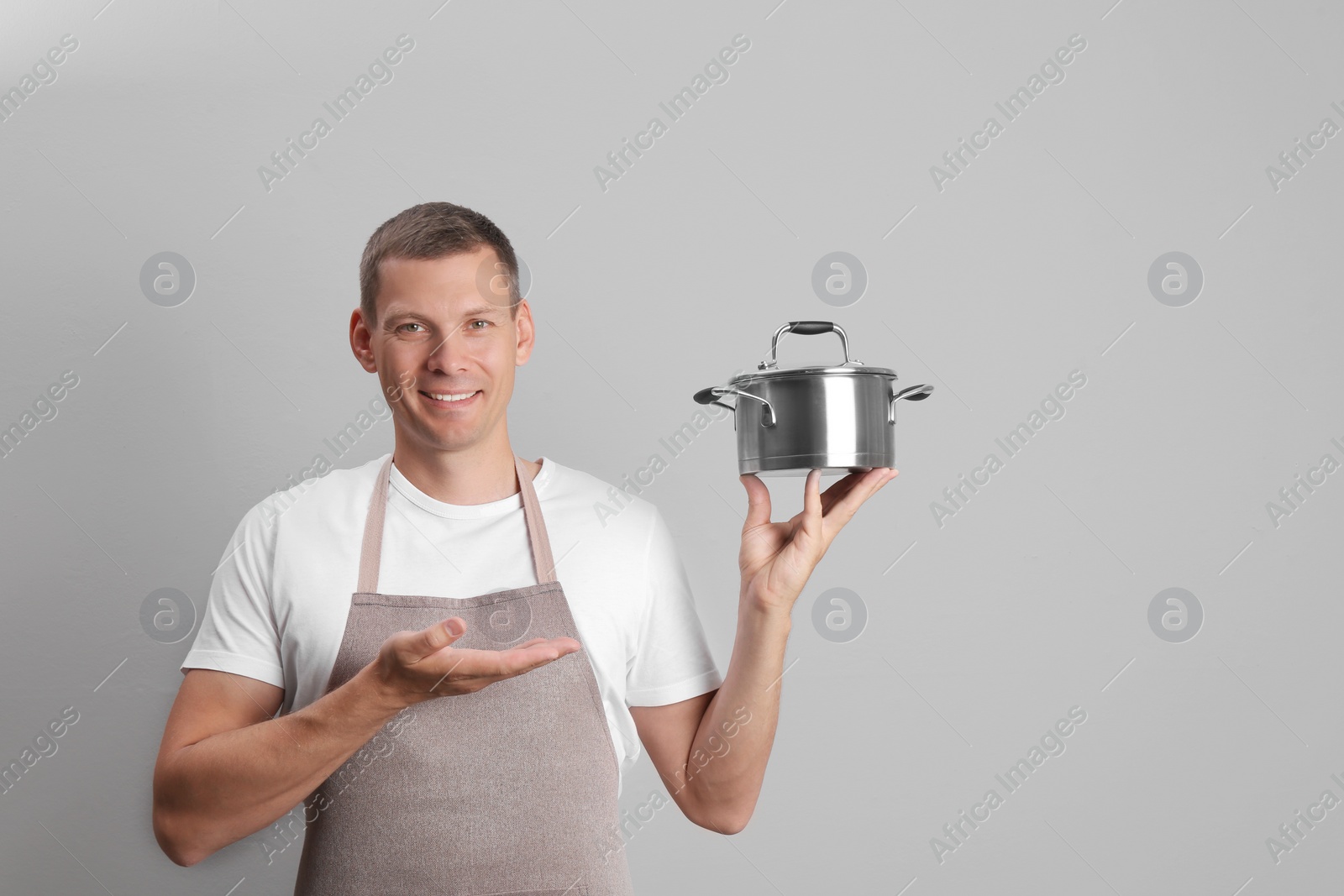Photo of Happy man with cooking pot on light grey background. Space for text