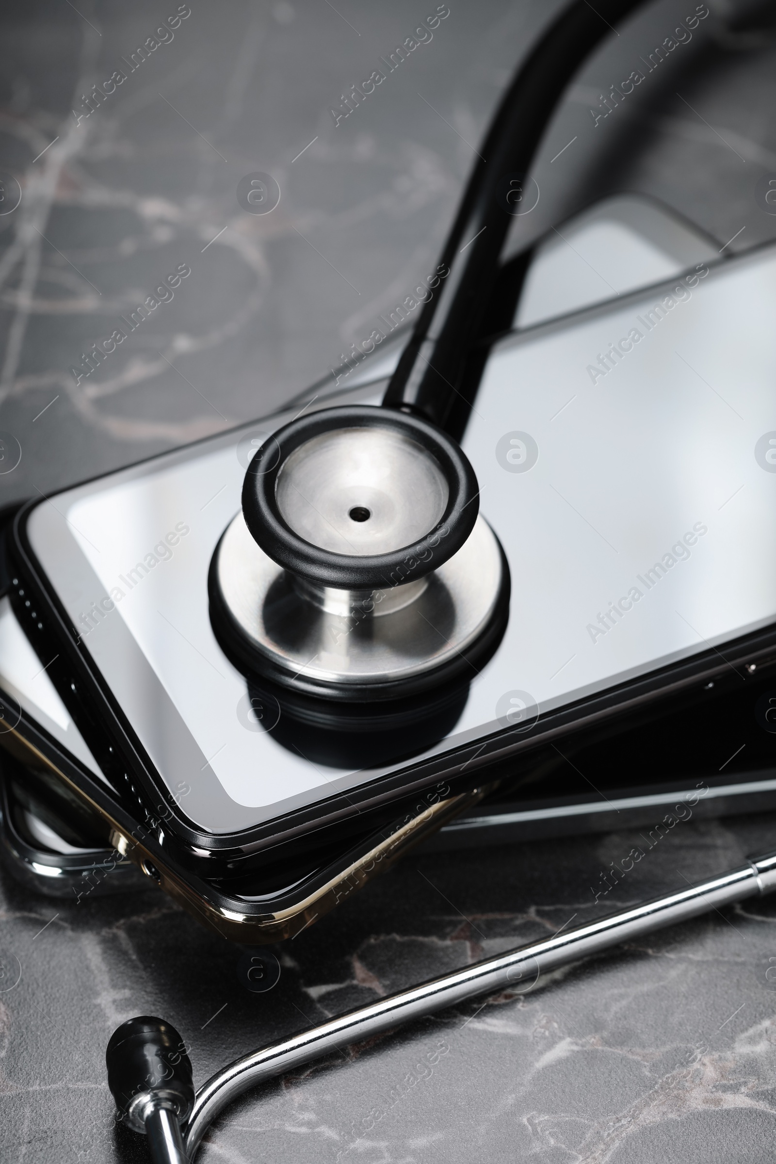 Photo of Stack of modern smartphones and stethoscope on black table, closeup