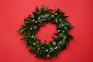 Photo of Beautiful handmade mistletoe wreath on red background, top view. Traditional Christmas decor