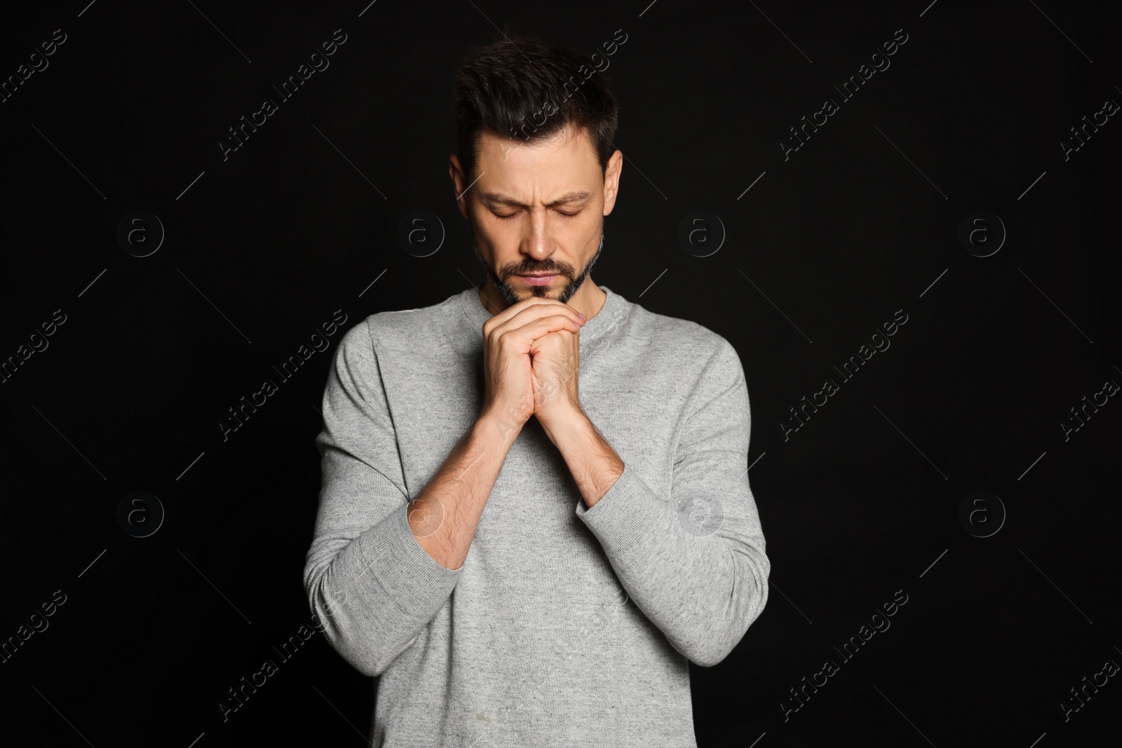 Photo of Man with clasped hands praying on black background