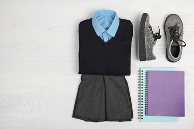 School uniform for girl and notebooks on white wooden background, top view