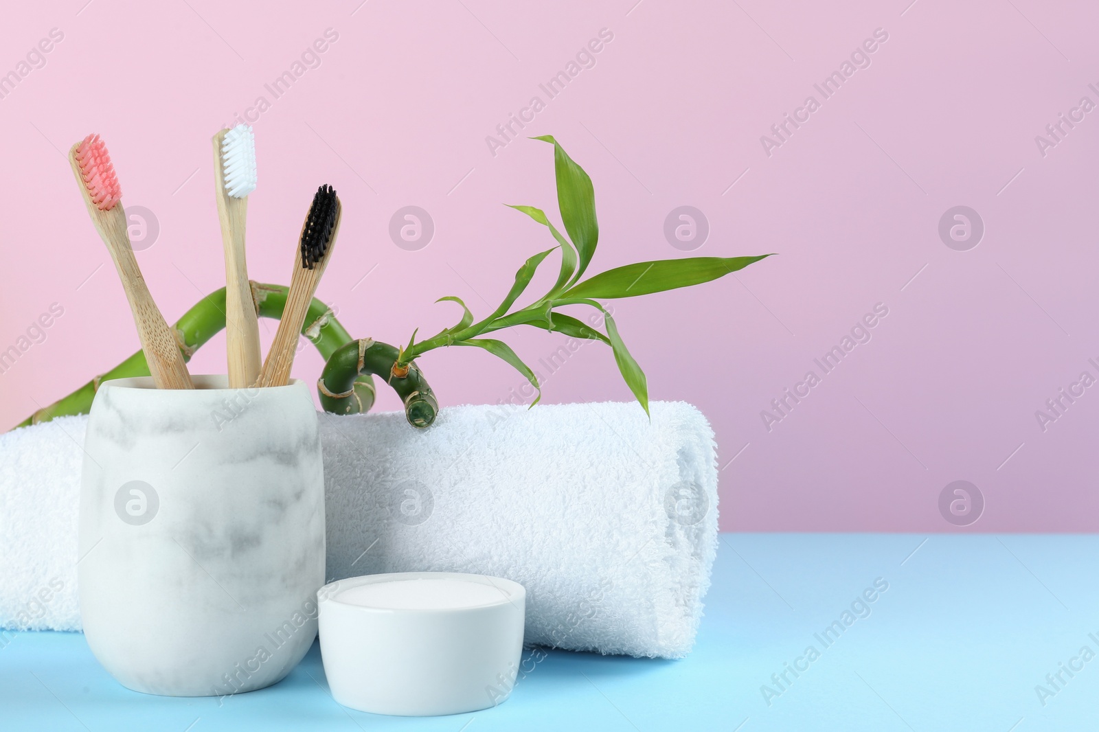 Photo of Bamboo toothbrushes, towel and bowl of baking soda on light blue table against pink background, space for text