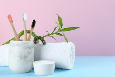 Bamboo toothbrushes, towel and bowl of baking soda on light blue table against pink background, space for text