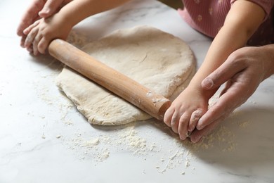 Photo of Father and child rolling raw dough at white table, closeup