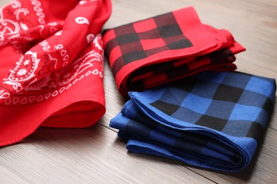 Stylish bandanas with different patterns on wooden table, closeup