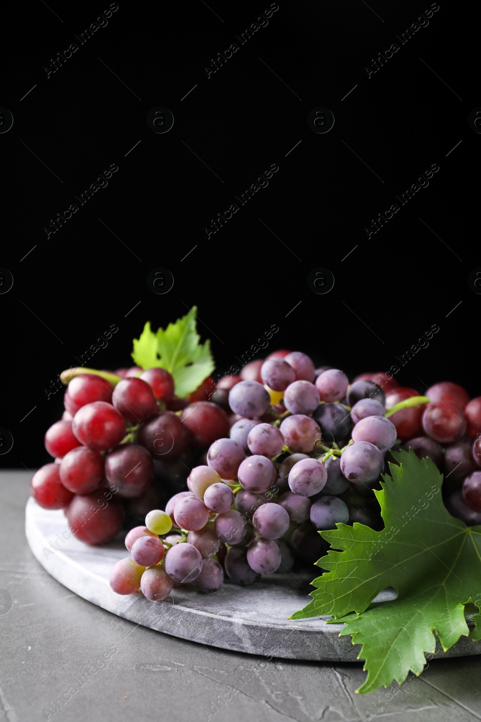 Photo of Fresh ripe juicy grapes on grey table against black background, space for text