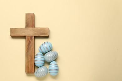 Wooden cross and painted Easter eggs on beige background, flat lay. Space for text