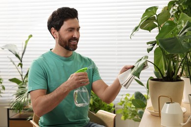 Man spraying beautiful potted houseplants with water indoors