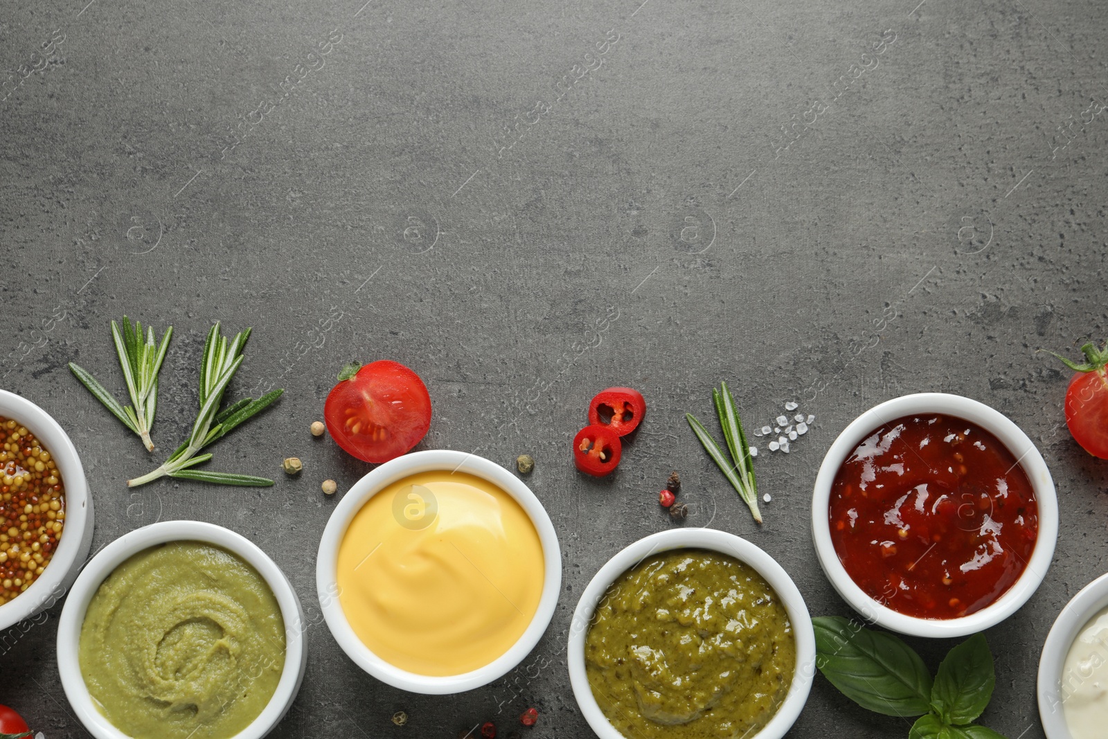 Photo of Bowls with different sauces and ingredients on gray background, flat lay. Space for text