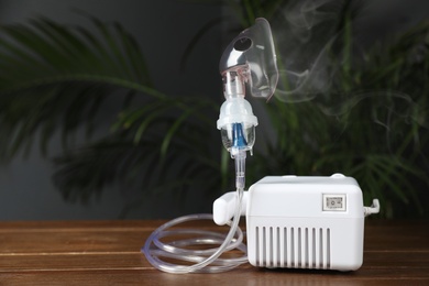 Image of Modern nebulizer with face mask on wooden table indoors. Inhalation equipment