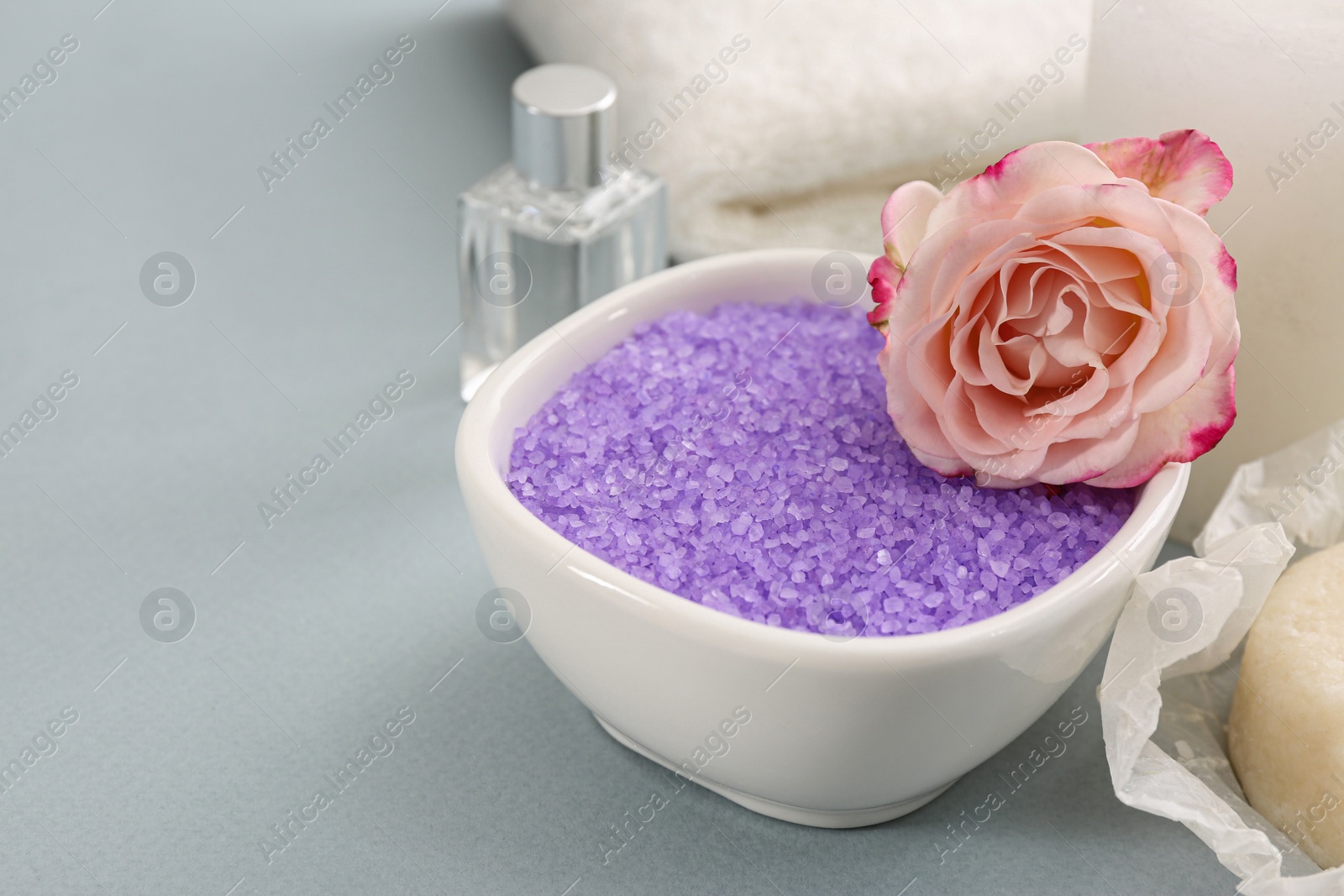 Photo of Bowl with sea salt and beautiful rose on light grey background, closeup. Space for text