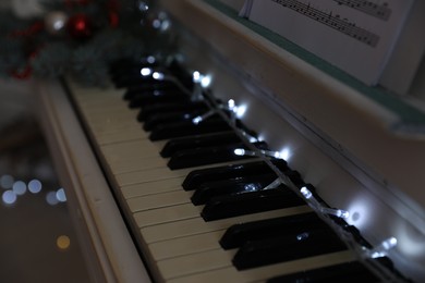 Photo of Glowing fairy lights on piano keys indoors, closeup. Christmas music