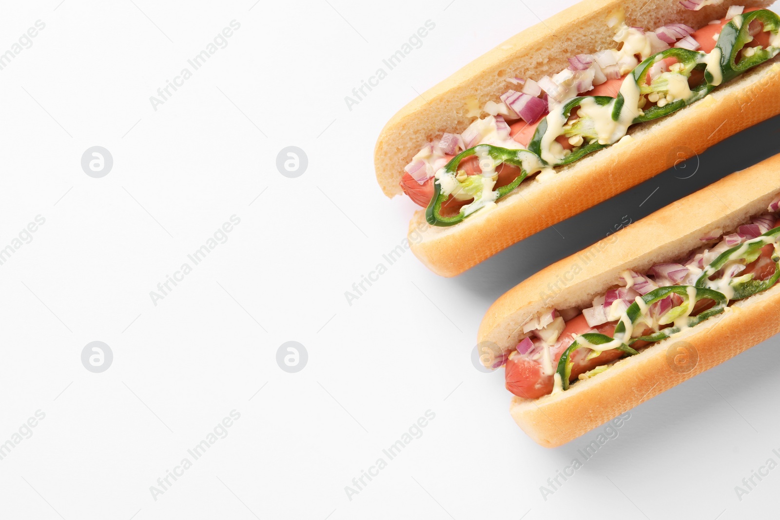 Photo of Delicious hot dogs with onion, chili pepper and sauce on white background, flat lay. Space for text