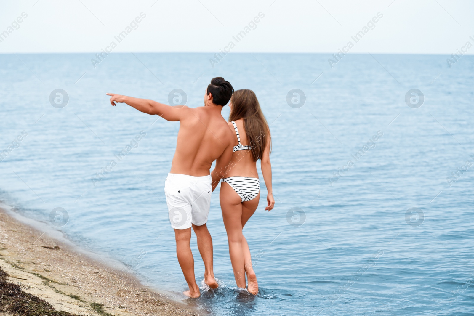 Photo of Happy young couple walking together on sea beach. Space for text