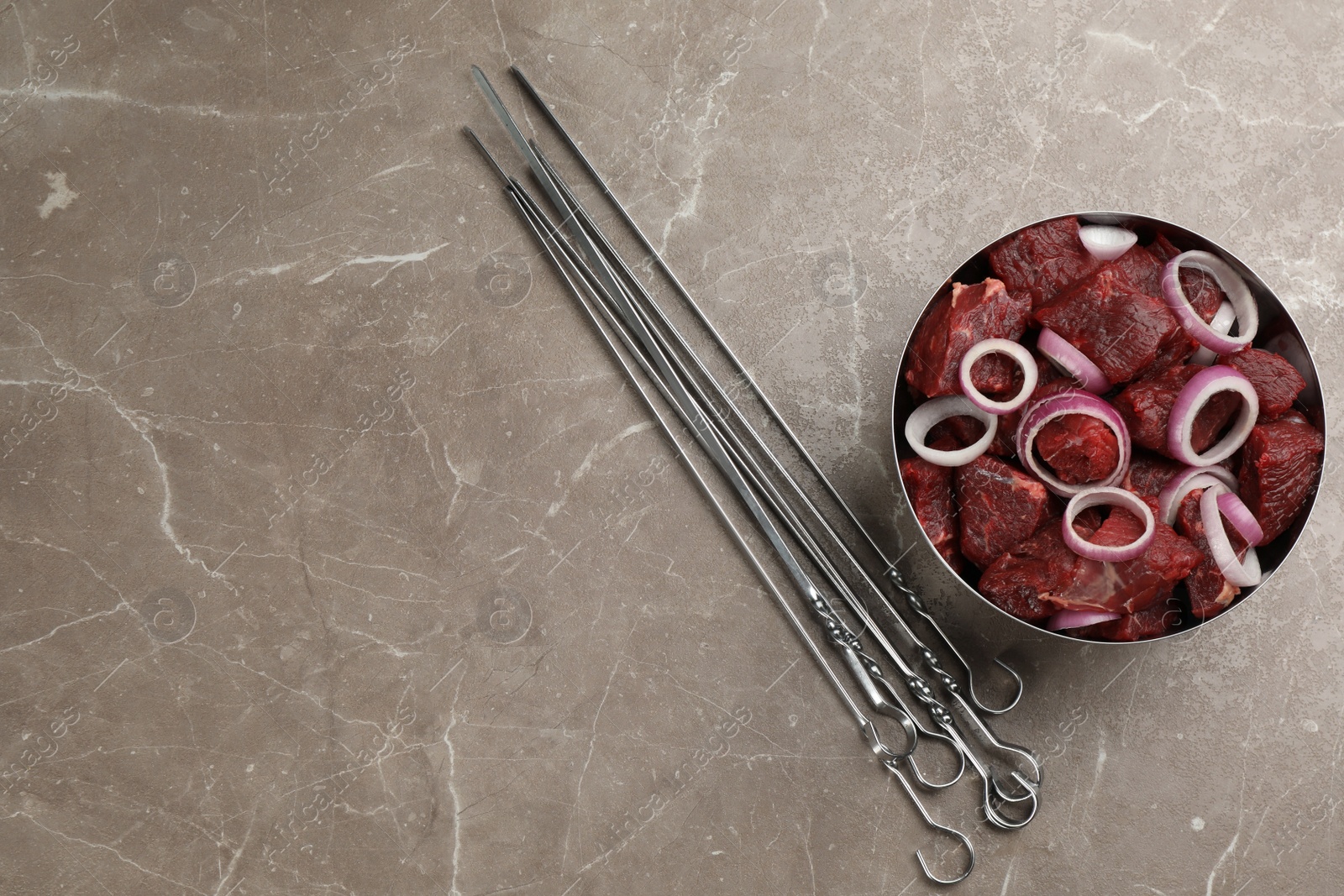 Photo of Metal skewers and bowl of raw meat with onion on marble table, flat lay. Space for text