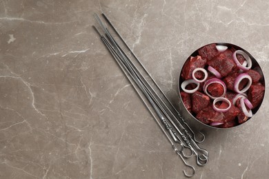 Photo of Metal skewers and bowl of raw meat with onion on marble table, flat lay. Space for text