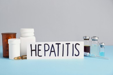 Photo of Word Hepatitis, vials and bottles of pills on light blue table