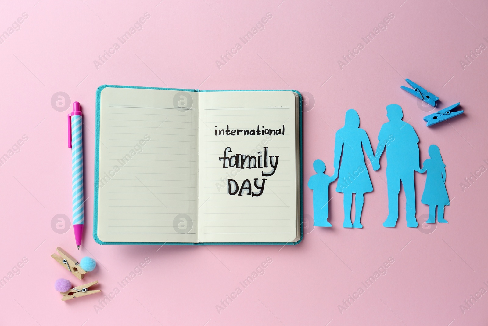 Photo of Happy International Family Day. Flat lay composition with notebook and paper people cutout on pink background