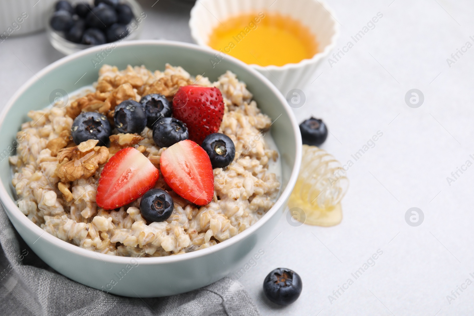 Photo of Tasty oatmeal with strawberries, blueberries and walnuts in bowl on grey table. Space for text