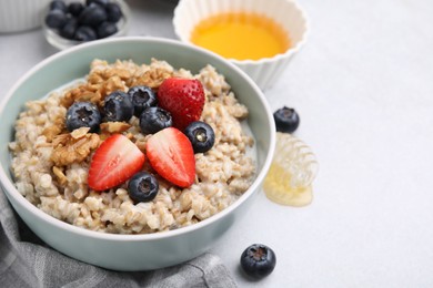 Photo of Tasty oatmeal with strawberries, blueberries and walnuts in bowl on grey table. Space for text