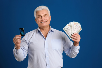 Happy senior man with cash money and credit card on blue background