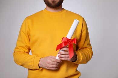 Student with diploma on light grey background, closeup