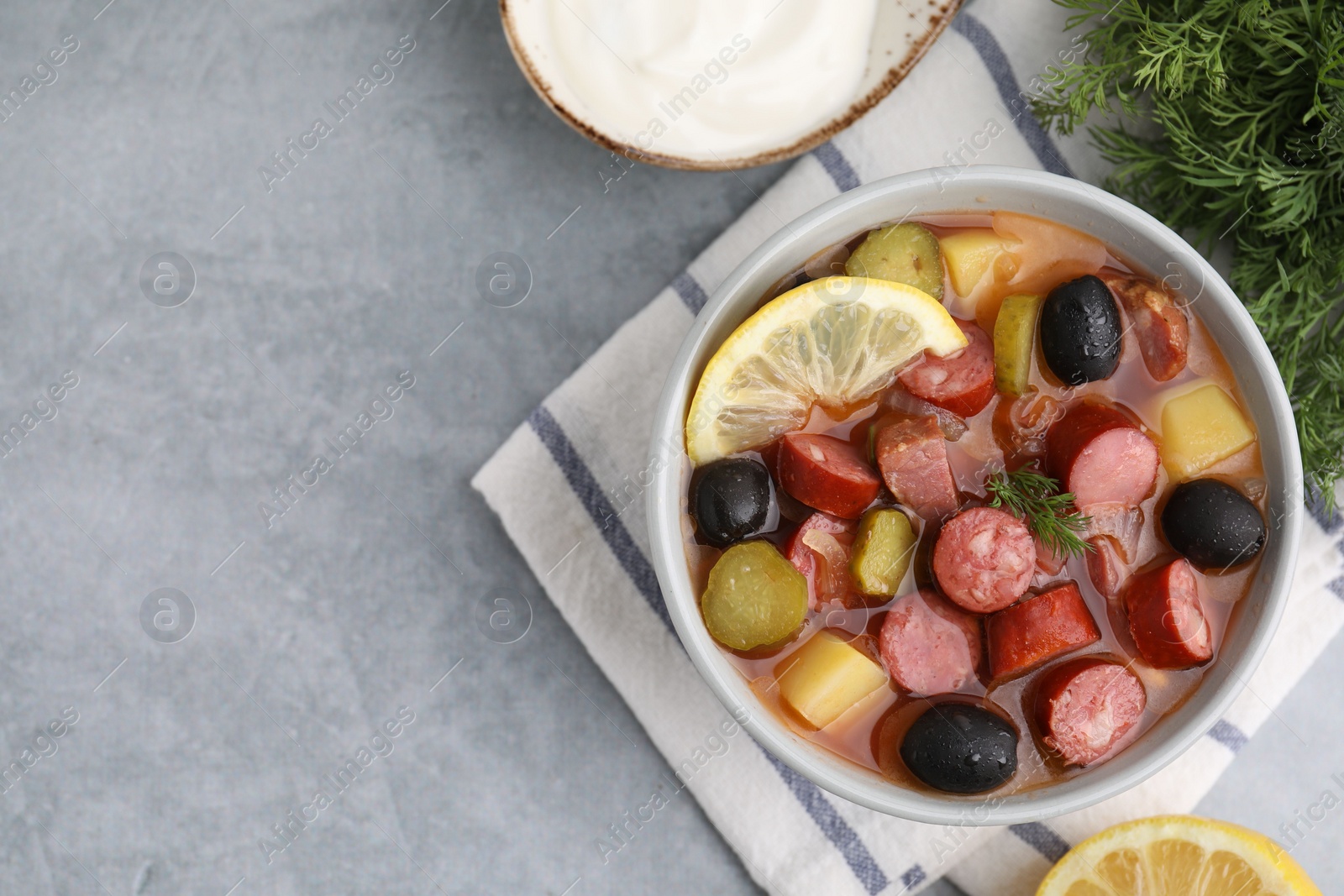 Photo of Meat solyanka soup with thin dry smoked sausages served on grey table, flat lay. Space for text