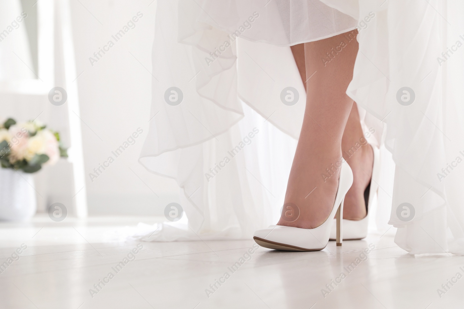 Photo of Young bride in beautiful wedding shoes walking indoors, closeup