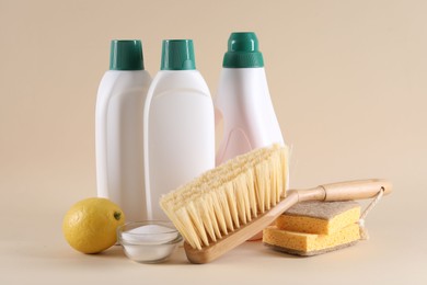 Bottles of cleaning product, sponges, brush, lemon and baking soda on beige background