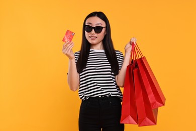 Photo of Happy woman with shopping bags and credit card on yellow background