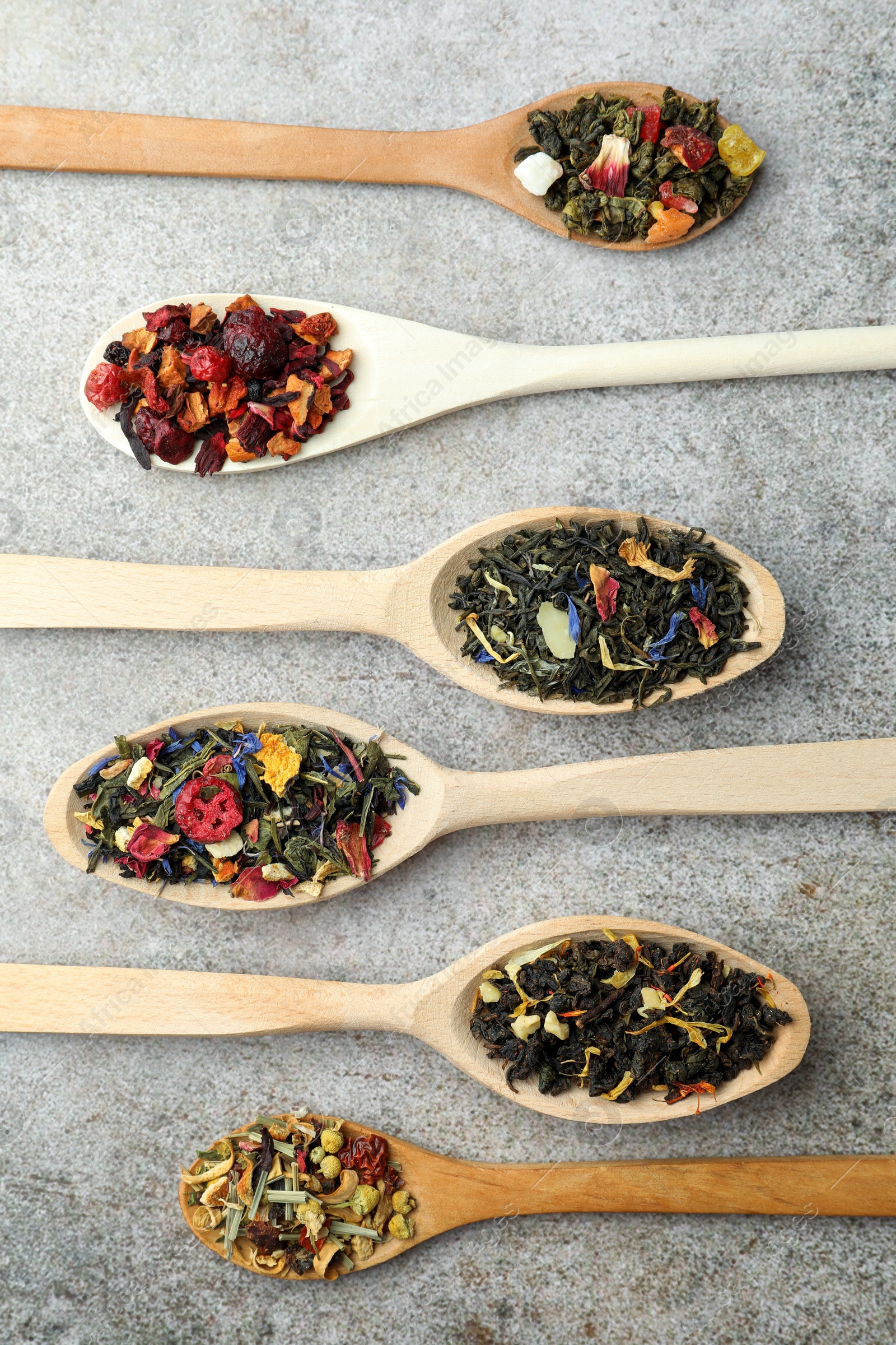 Photo of Different kinds of dry herbal tea in wooden spoons on light grey table, flat lay