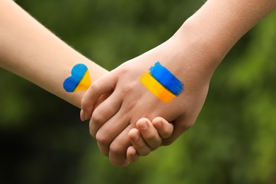 Stop war in Ukraine. Mother and her child holding hands, outdoors closeup. Drawings with colors of Ukrainian flag