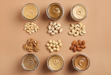 Many tasty nut butters in jars and nuts on beige table, flat lay